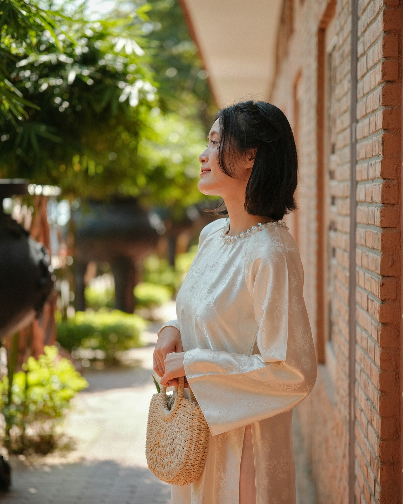 Cream flowing dress with a beaded necklace detail at the collar, carrying a small woven straw bag