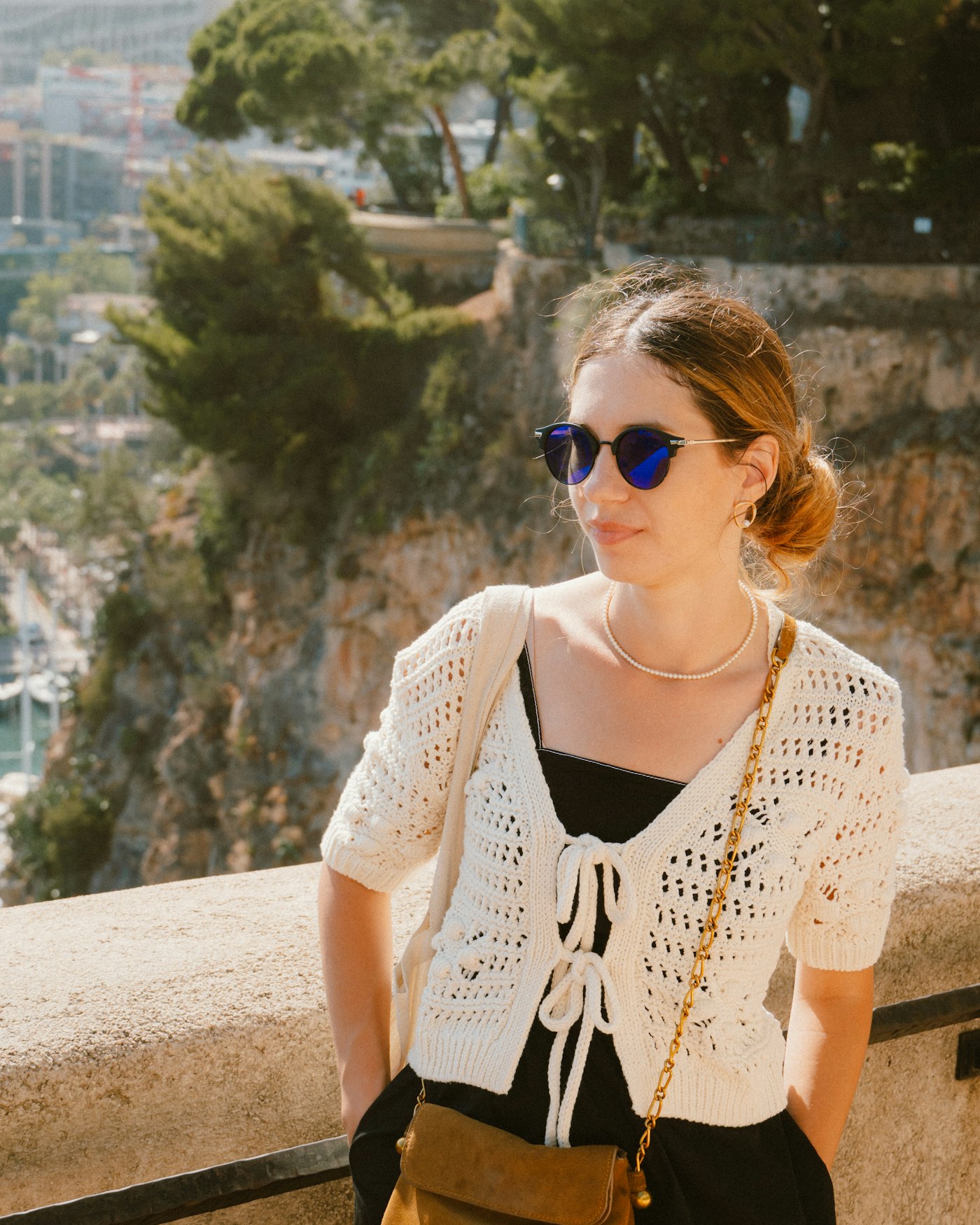 Black slip dress layered under a cream crochet cardigan with a tan suede crossbody bag