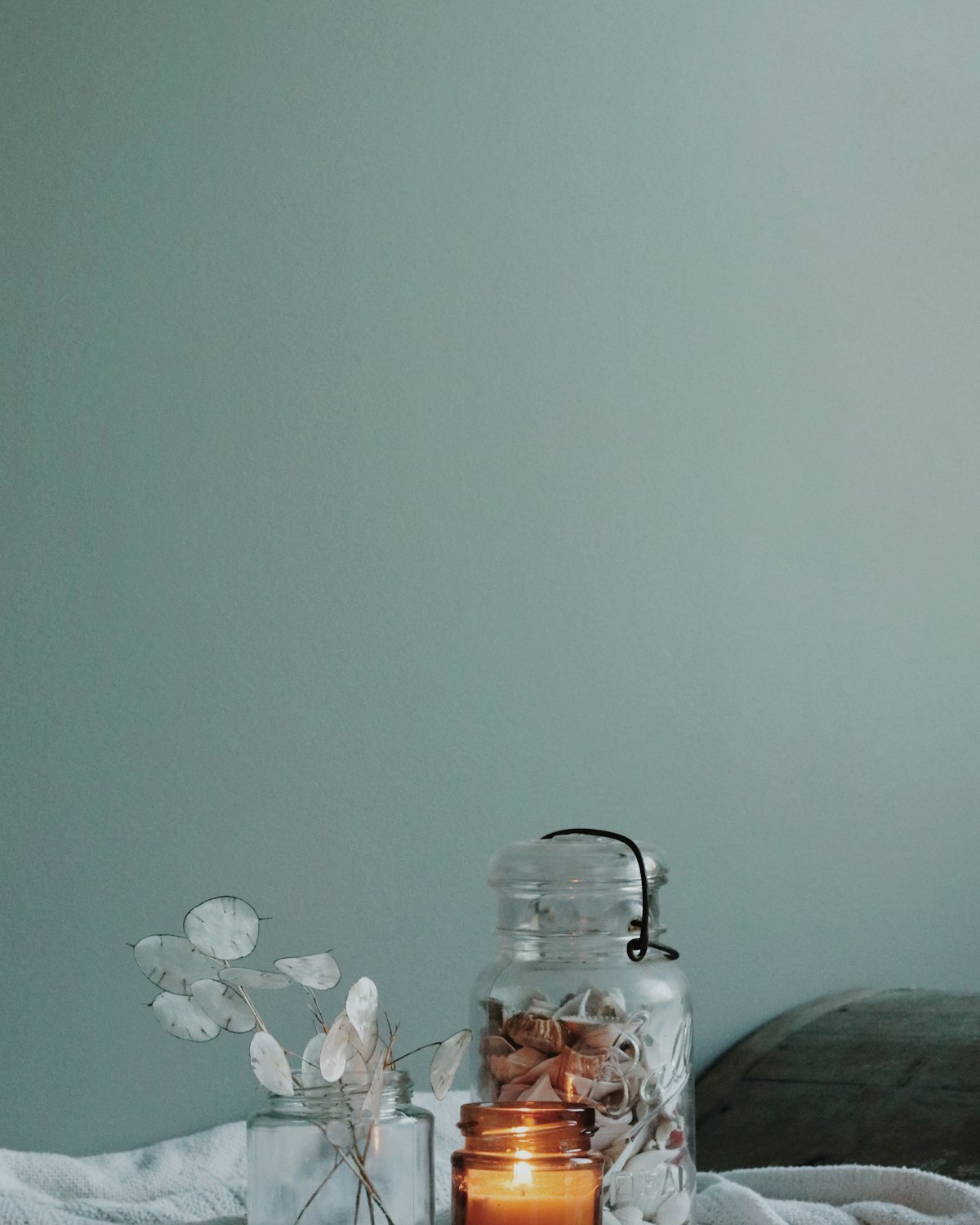 Cream glass candle with a plain paper label, lid resting beside it